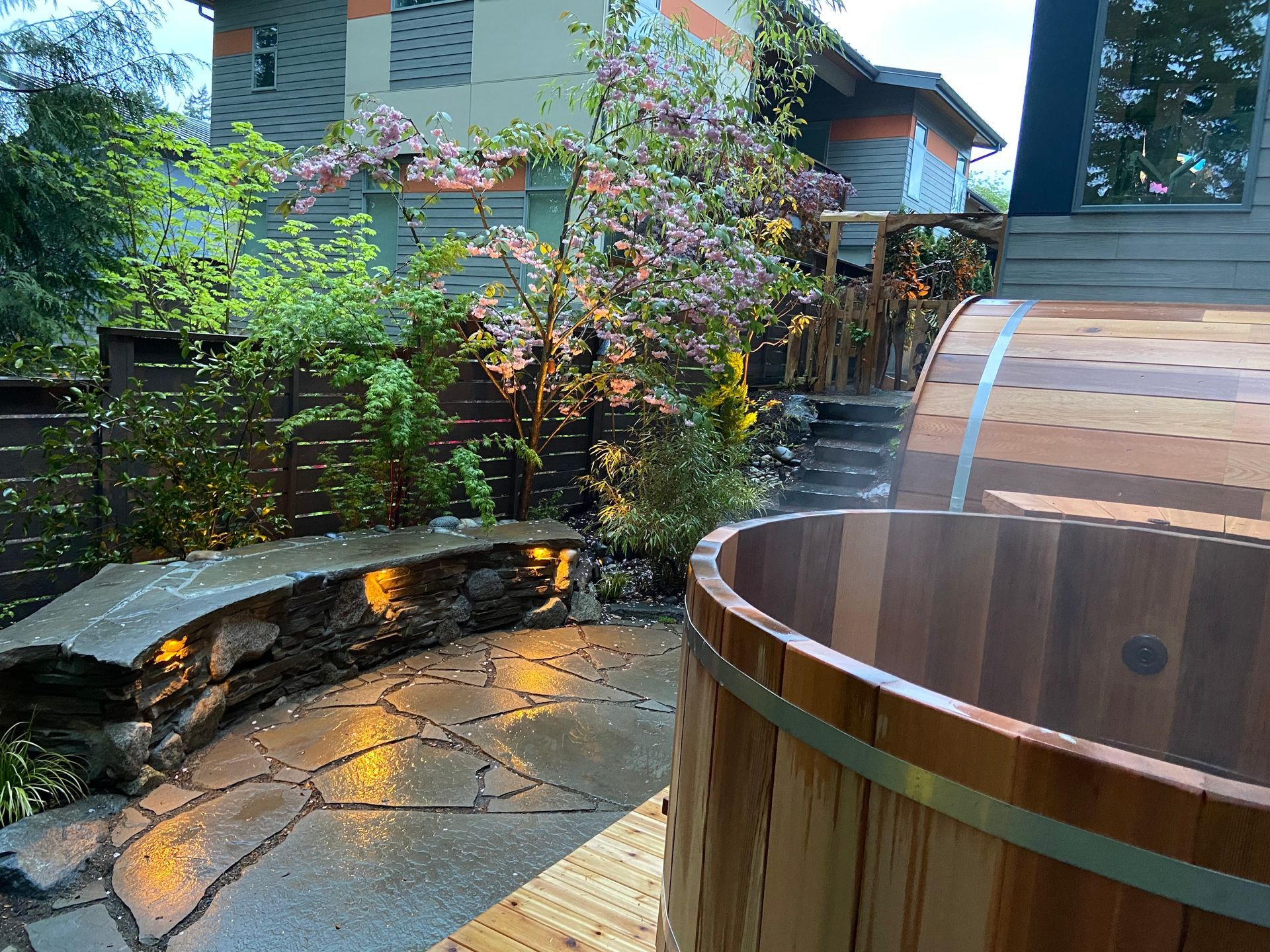 A wooden hot tub is sitting on a patio next to a house.