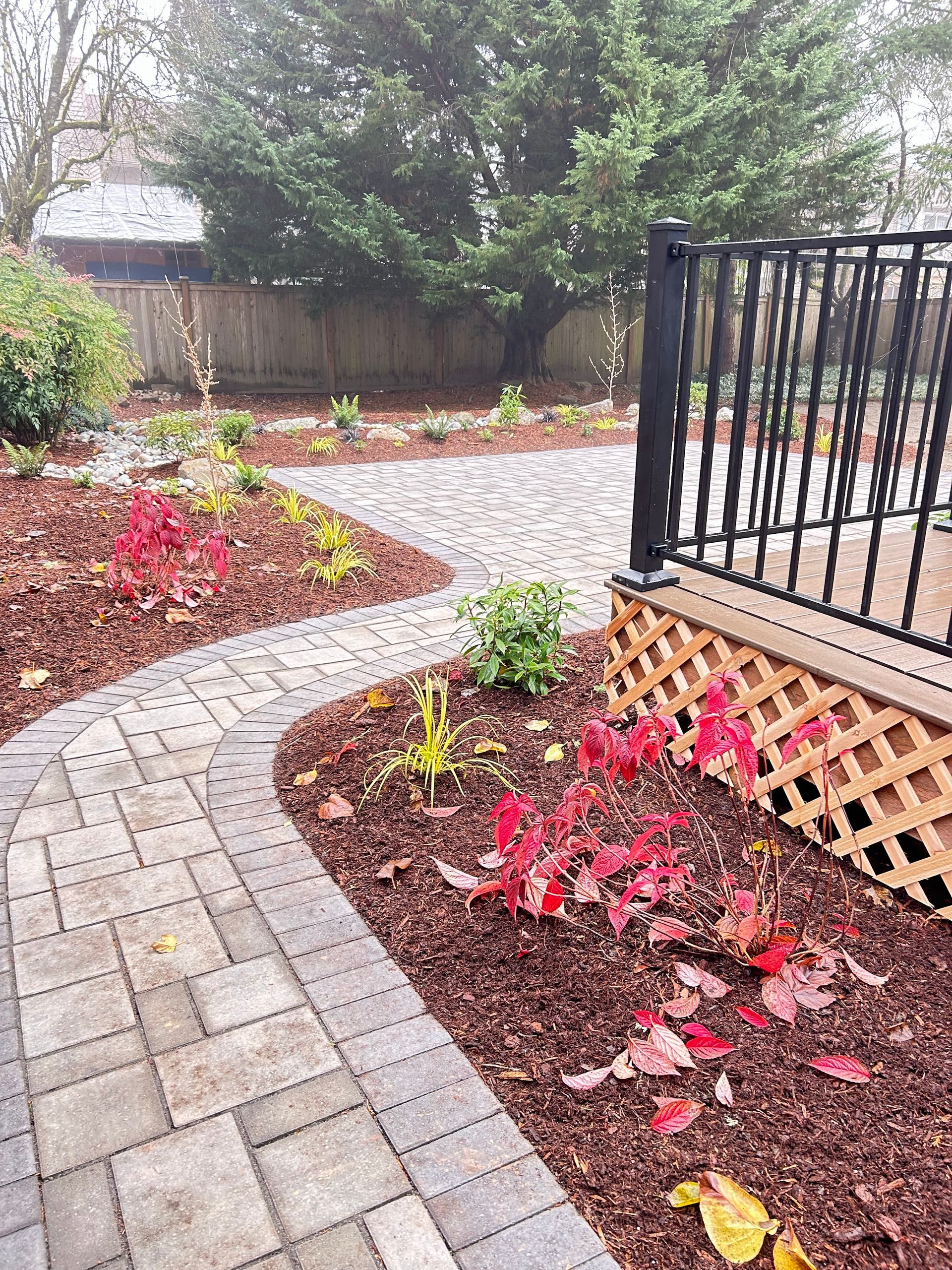 A brick walkway leading to a deck with leaves on the ground.