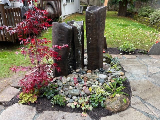 A large rock patio with a wheelbarrow in the background.