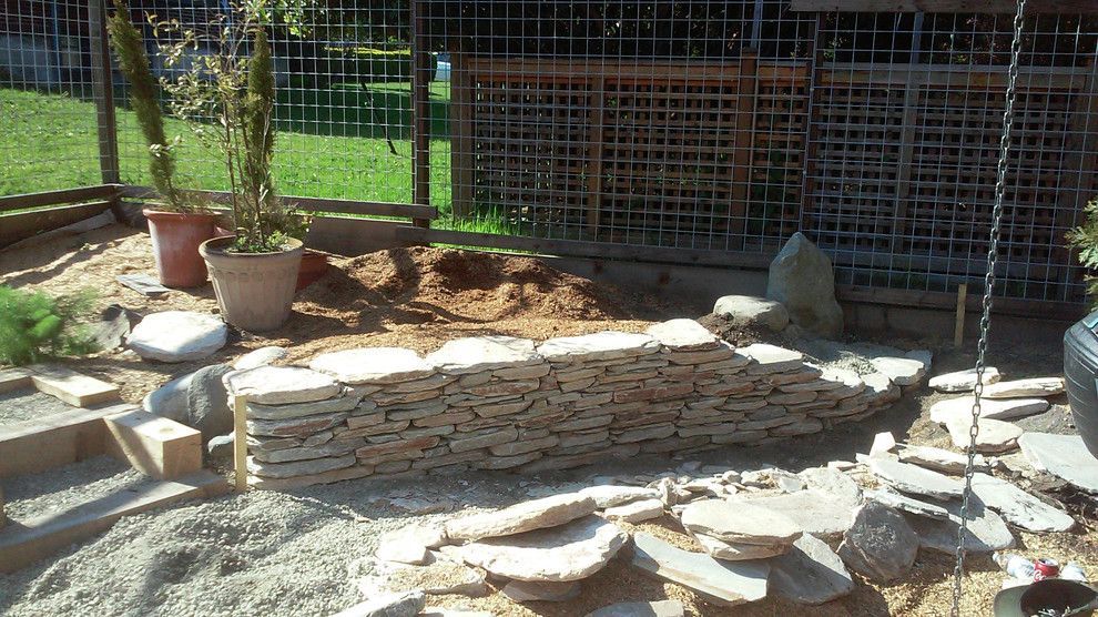 A stone wall is being built in a garden with a fence in the background.