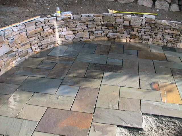 A stone wall is surrounding a patio with tiles