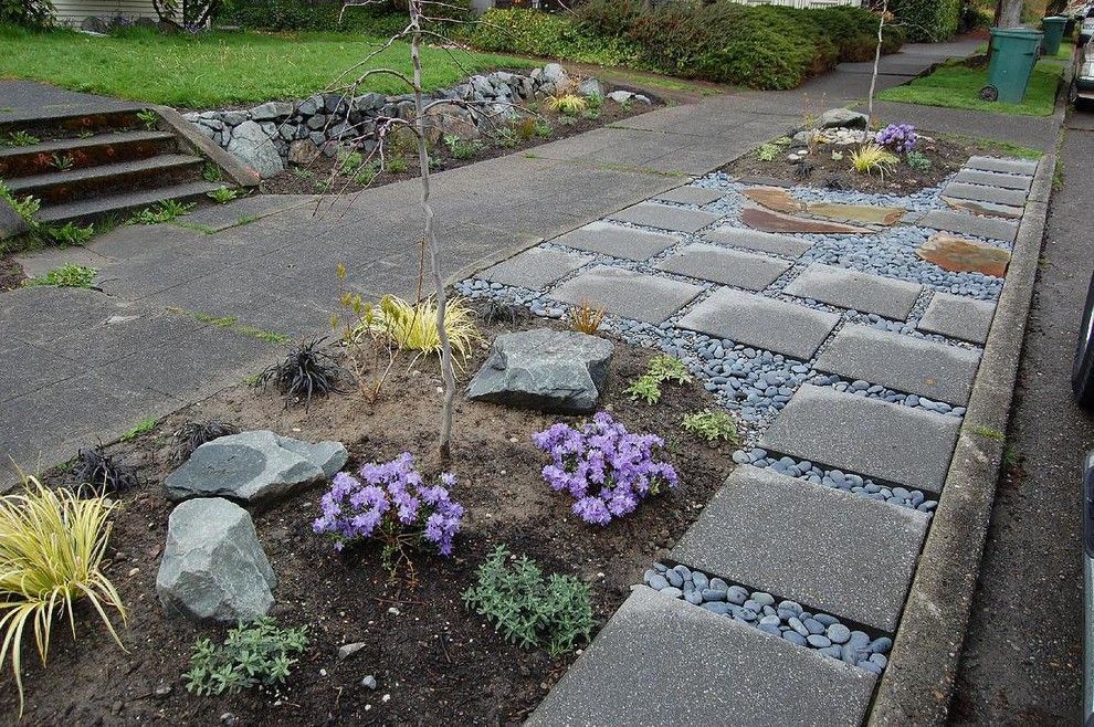 A garden with purple flowers and rocks along a sidewalk