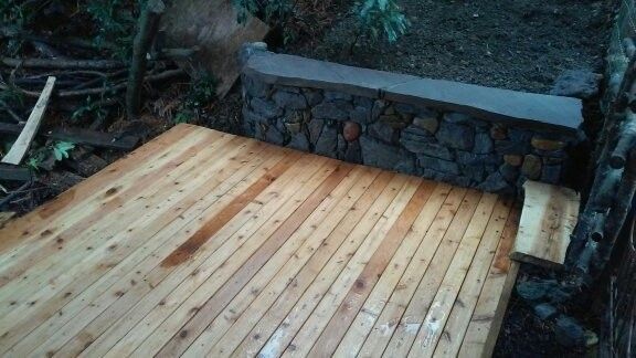 A wooden deck is sitting next to a stone wall.