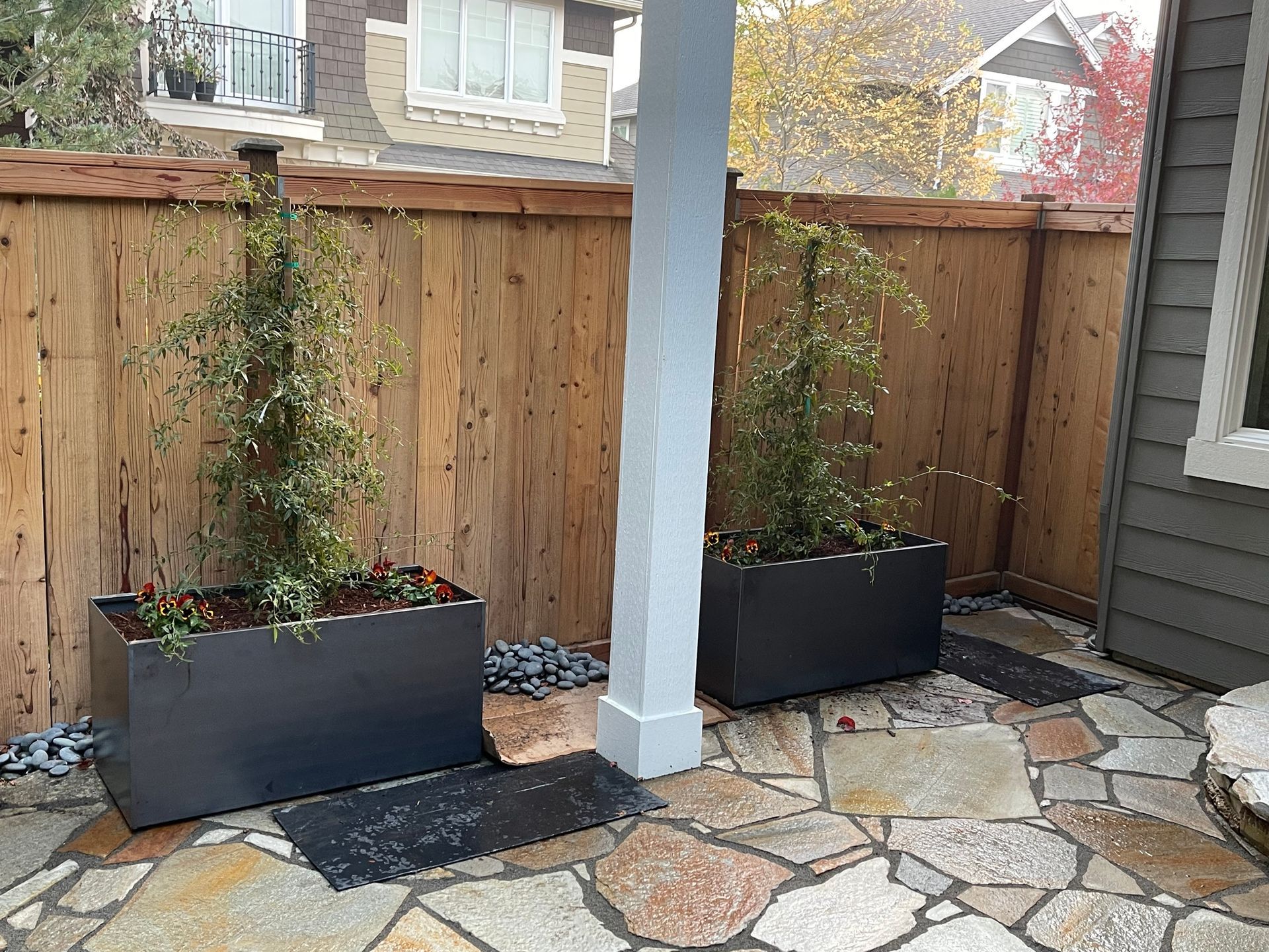 Two planters are sitting on a stone patio next to a wooden fence.