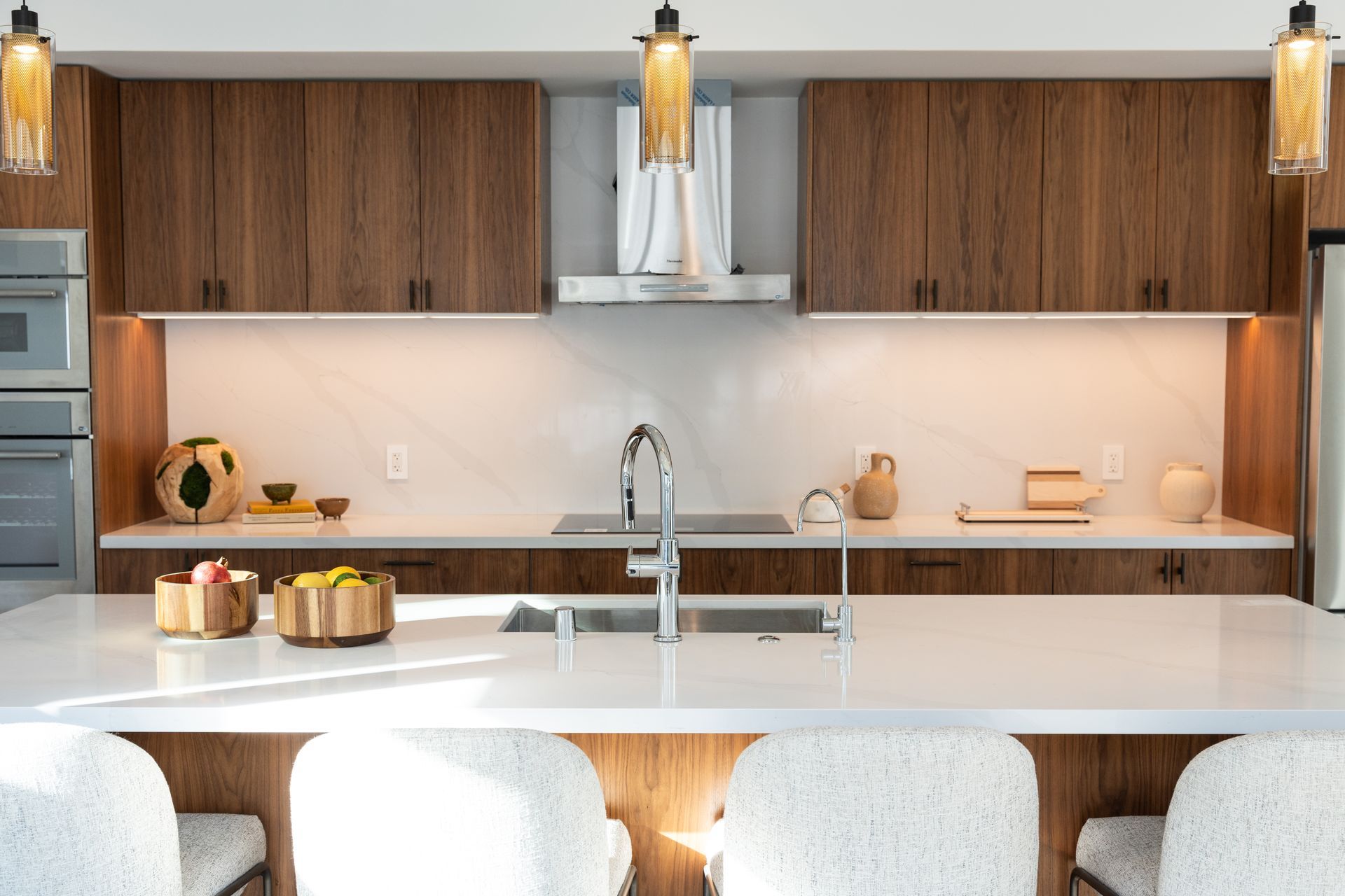 Modern kitchen with wood cabinets, white countertops, and decorative pendant lights above a large island with seating.