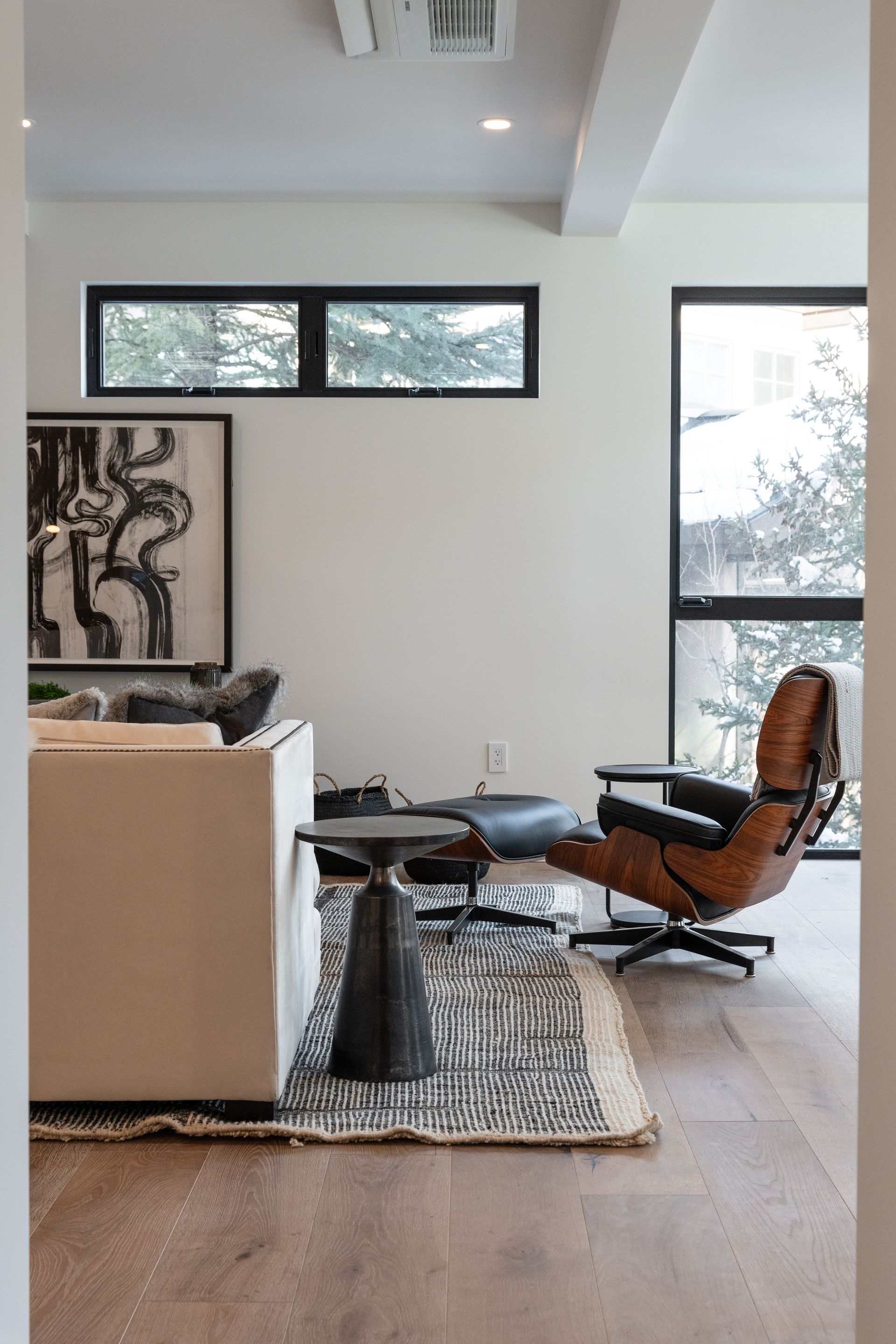Living room with modern furniture, including a leather chair, small table, and rug, framed by large windows.