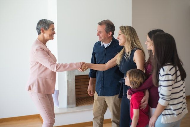 A property manager in a pink suit shaking hands with someone who is standing with their spouse and three children