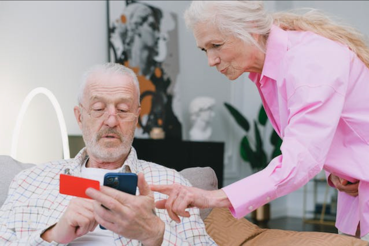 two elderly people looking at a cellphone with a credit card in one hand