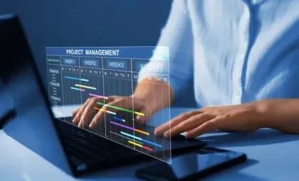 A person is typing on a laptop computer with a project management chart on the screen.