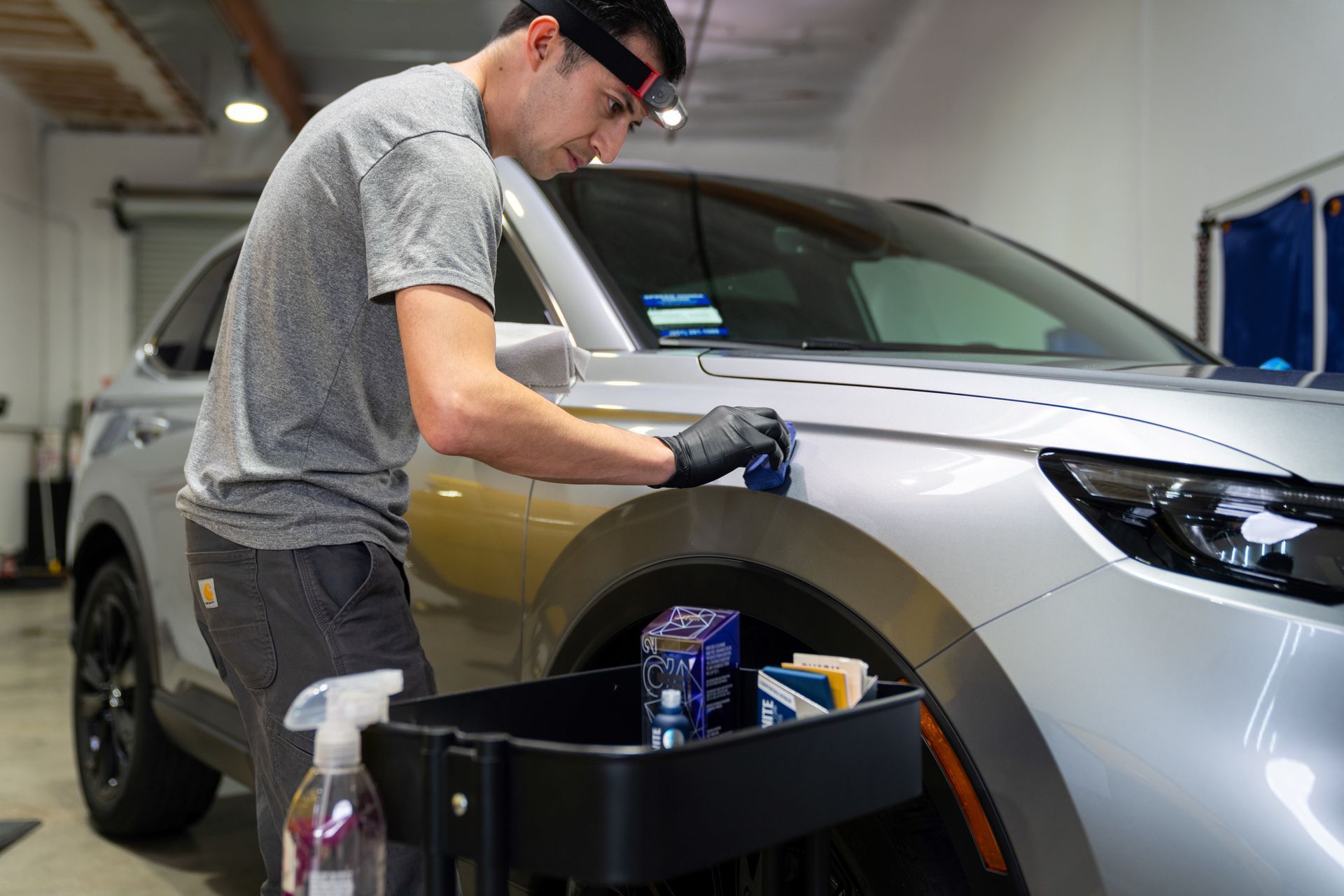 A man is applying Gyeon Ceramic Coating on the fender of a car in a garage .