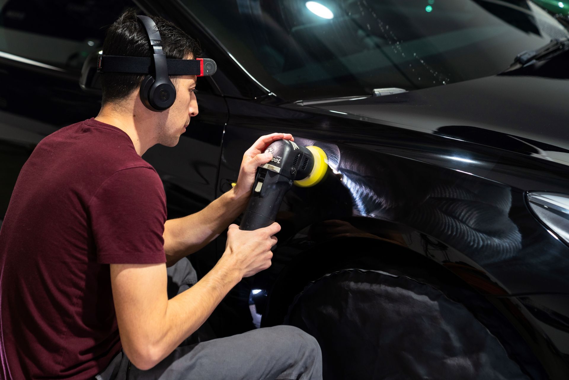 A man wearing headphones is paint polishing a black Tesla car .