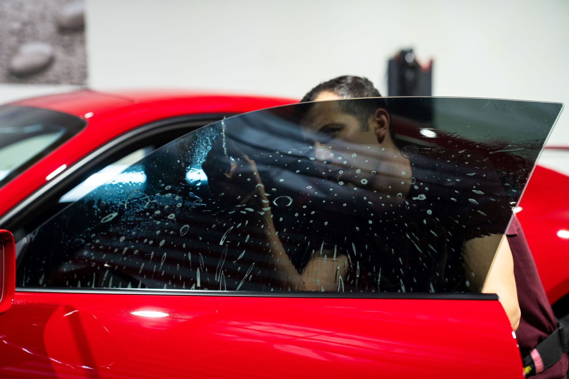 A man is applying window tinting to a red Porsche 911 car .