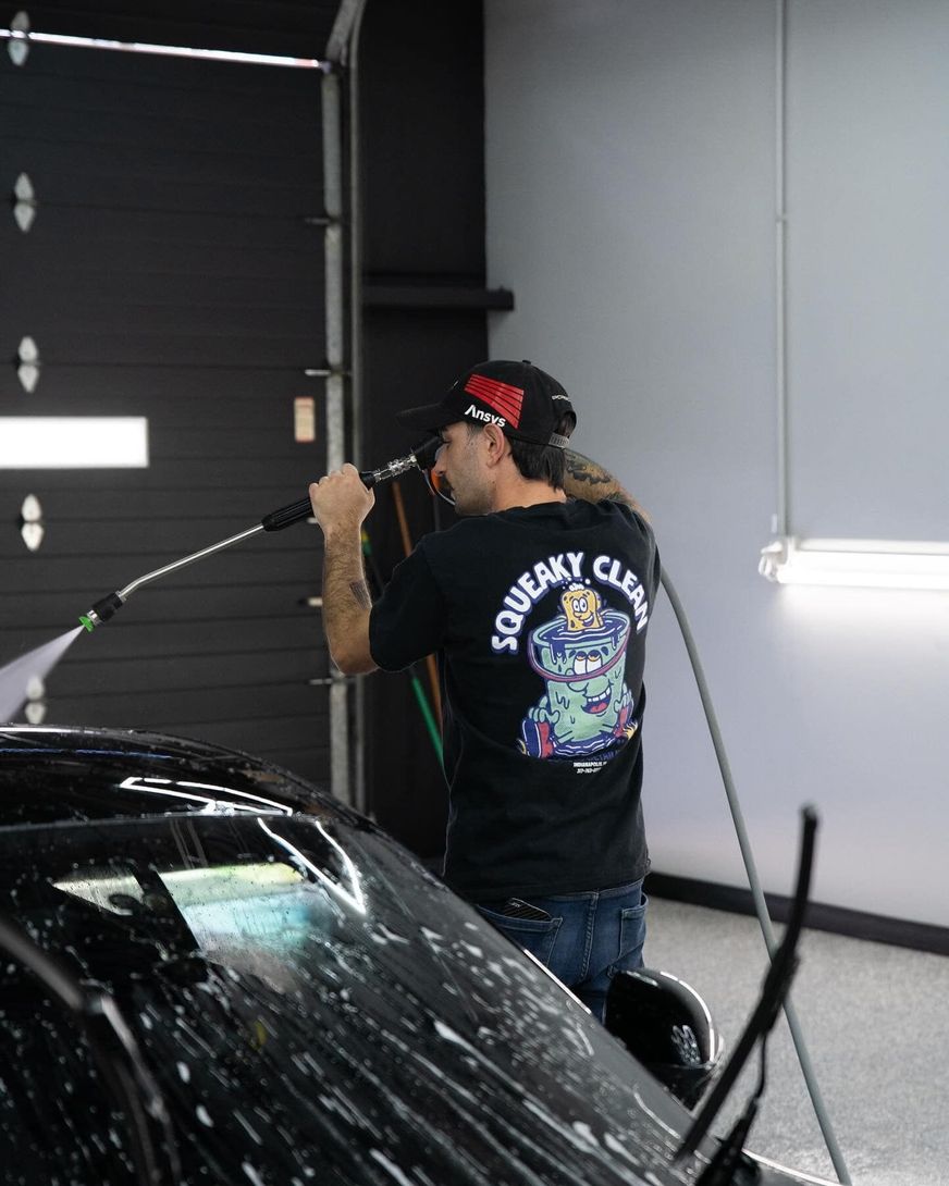 A man is washing a car with a squeaky clean shirt on