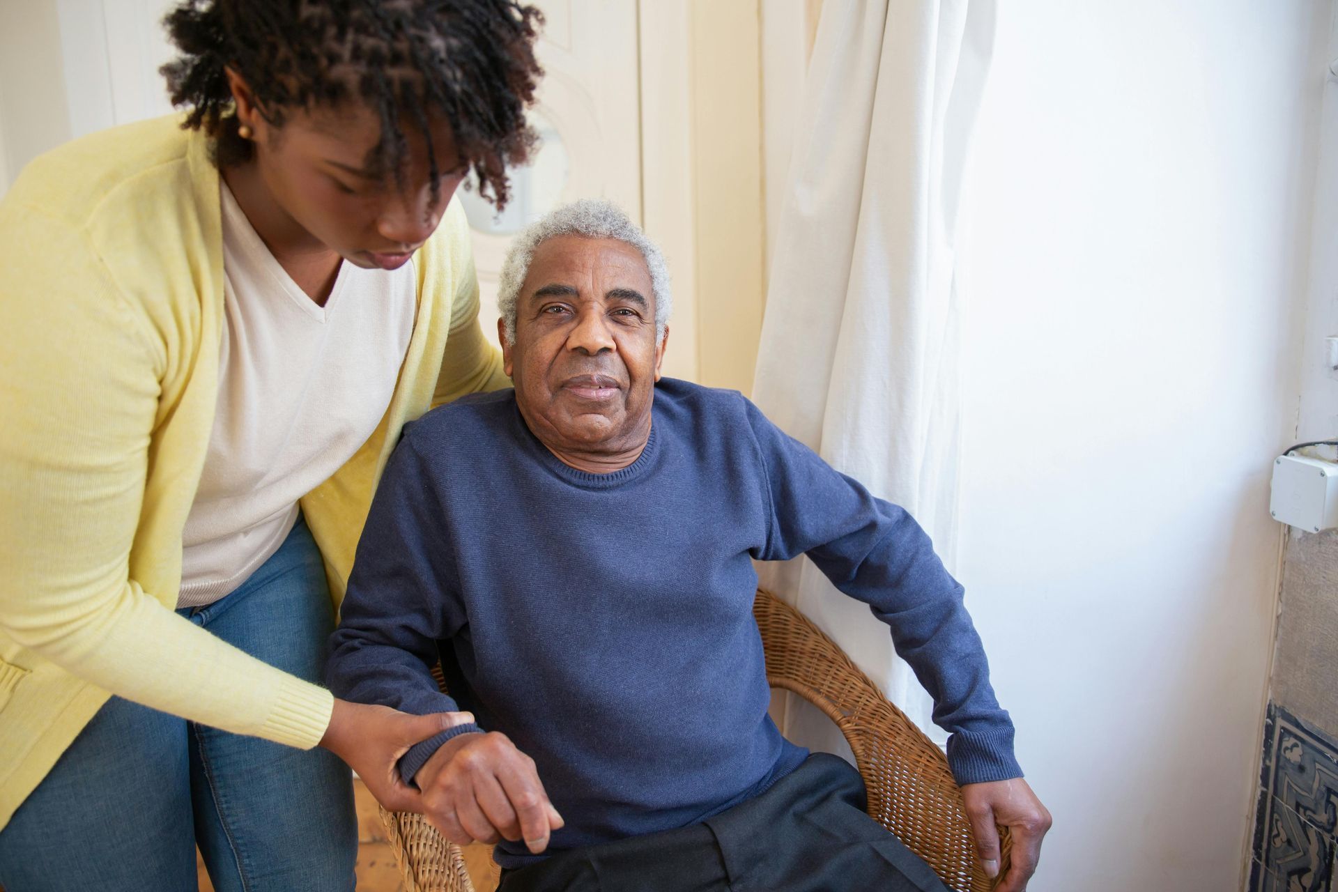 A woman is helping an elderly man sit in a chair.