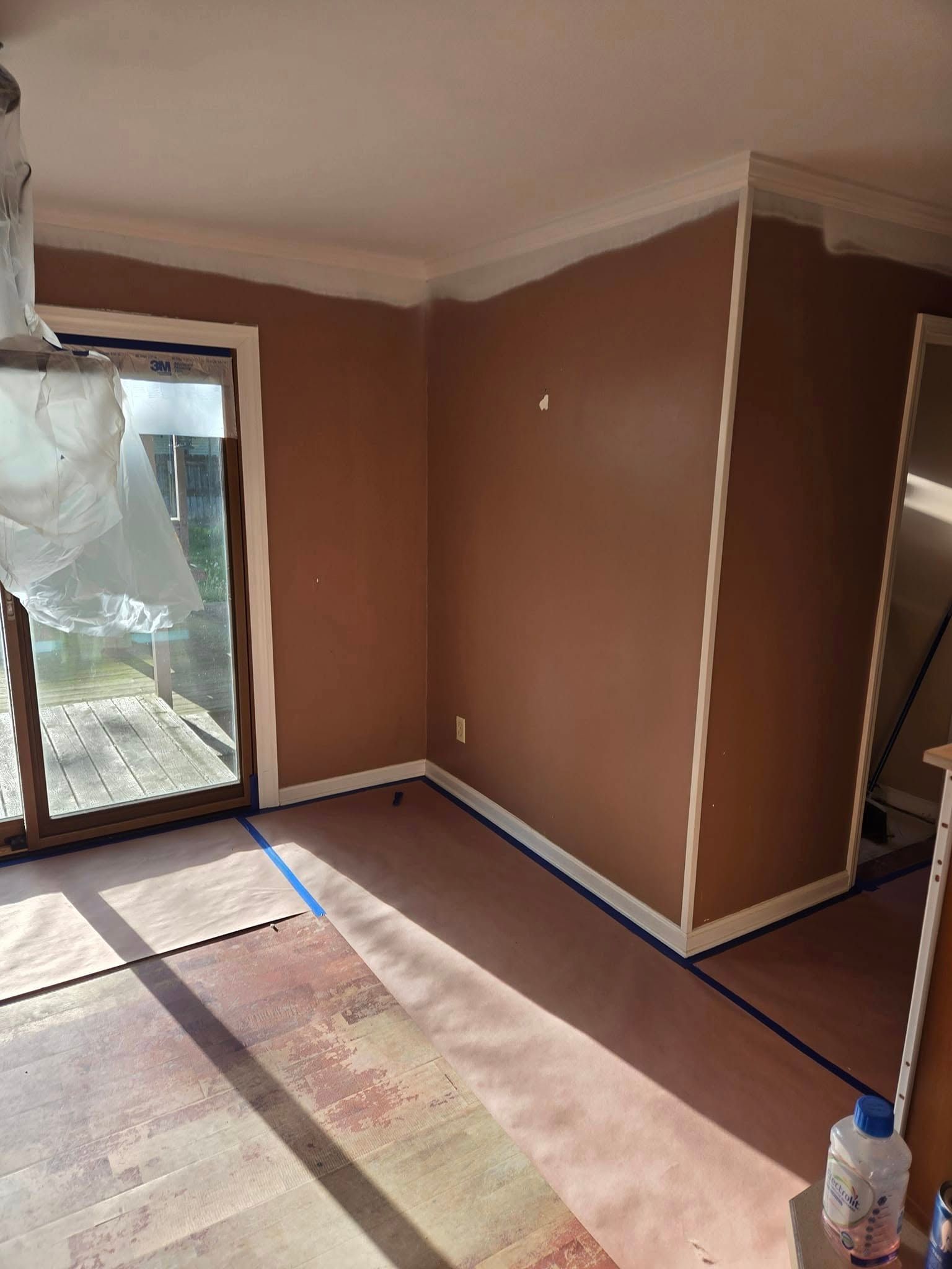 A room with brown walls and a sliding glass door is being painted.