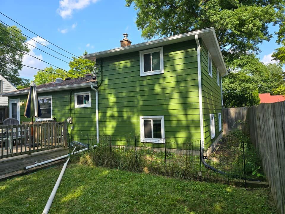 A green house with a deck and a fence in the backyard.