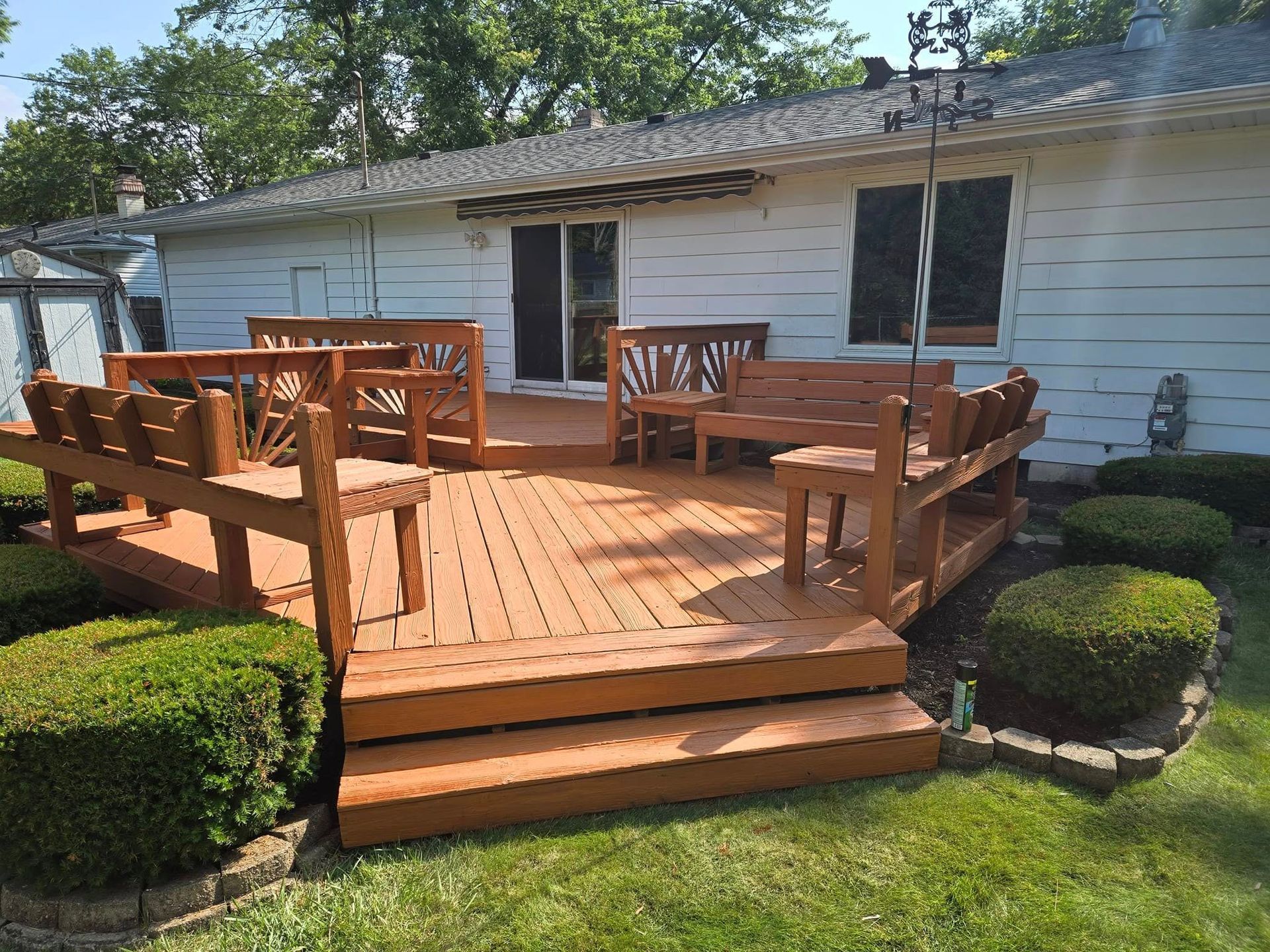 A wooden deck with a bench and chairs in front of a white house.