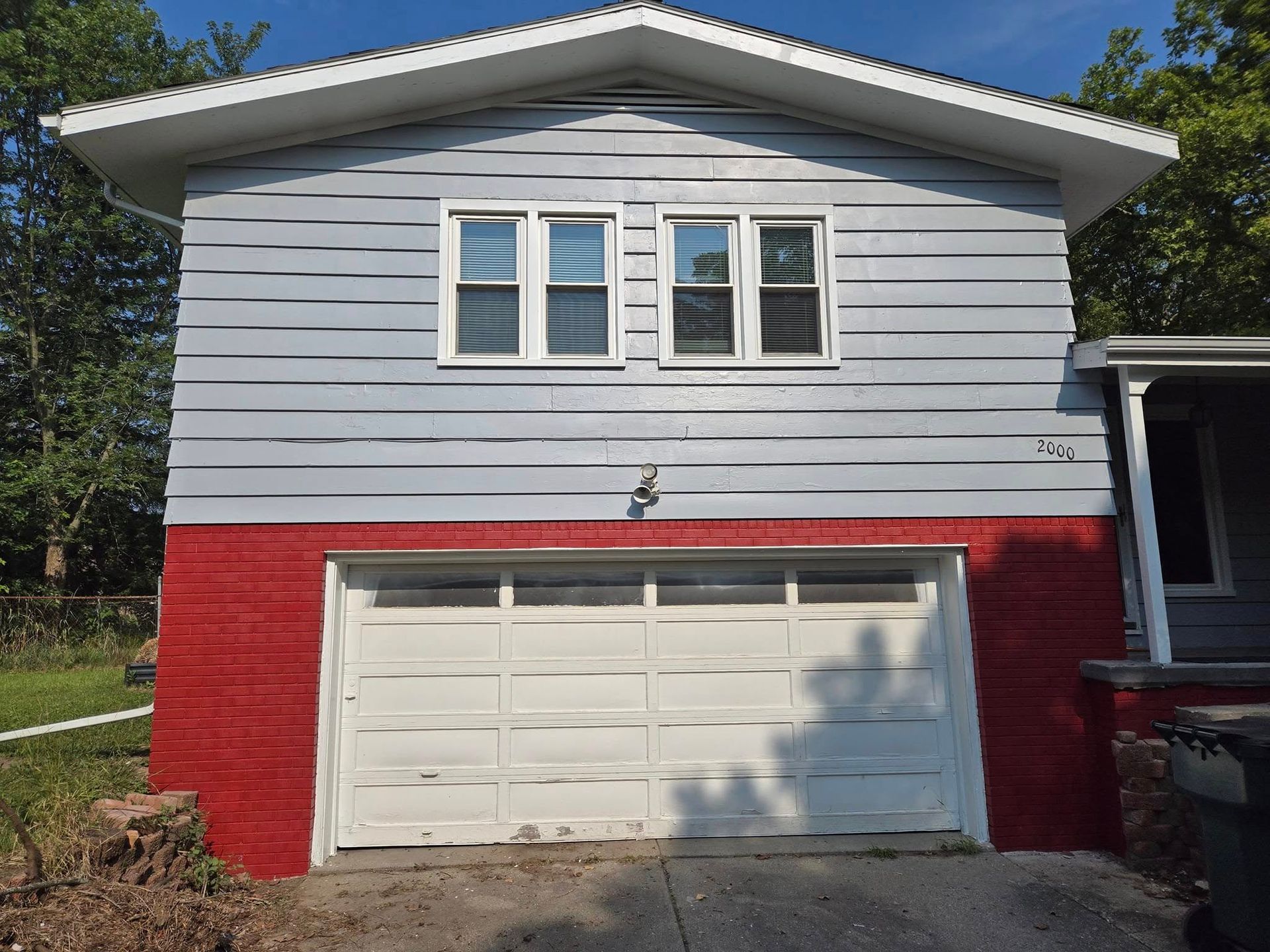 A gray house with a red trim and a white garage door.