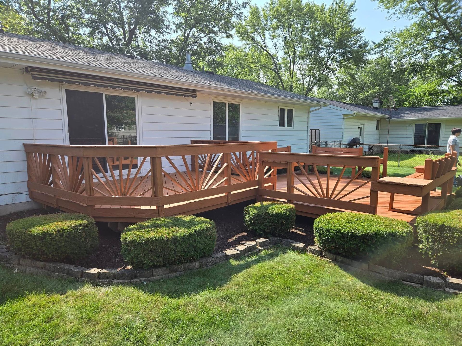A wooden deck with a bench and chairs in front of a white house.