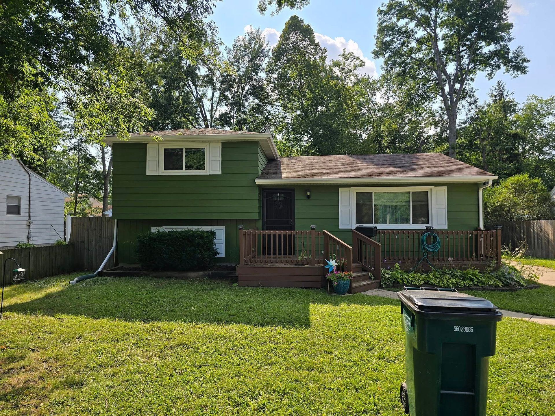 A green house with a trash can in front of it.