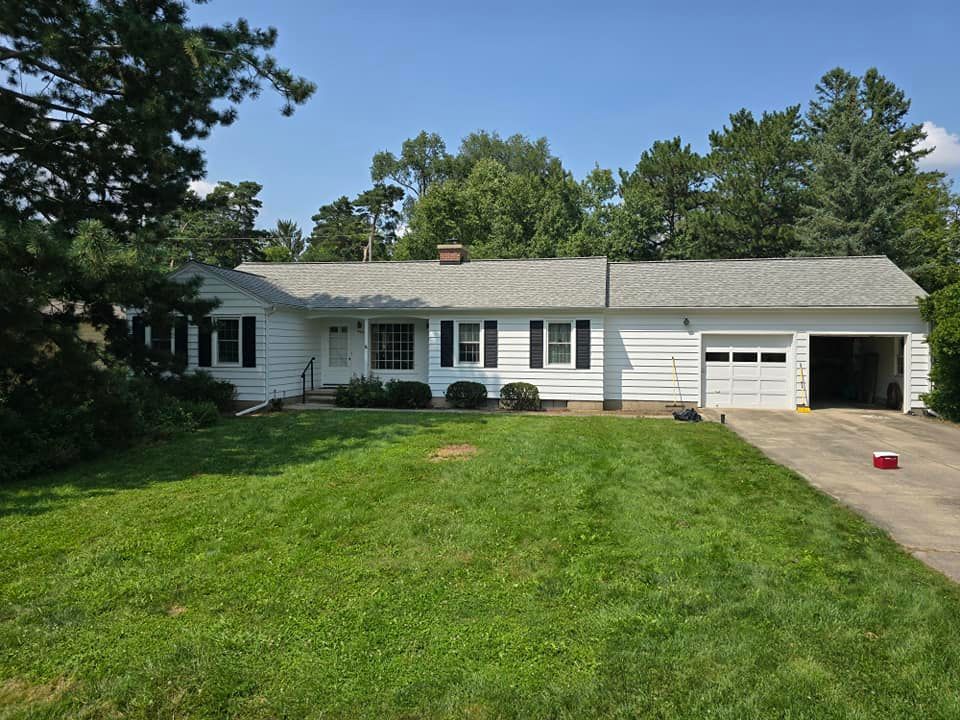 A white house with a gray roof and a large lawn in front of it