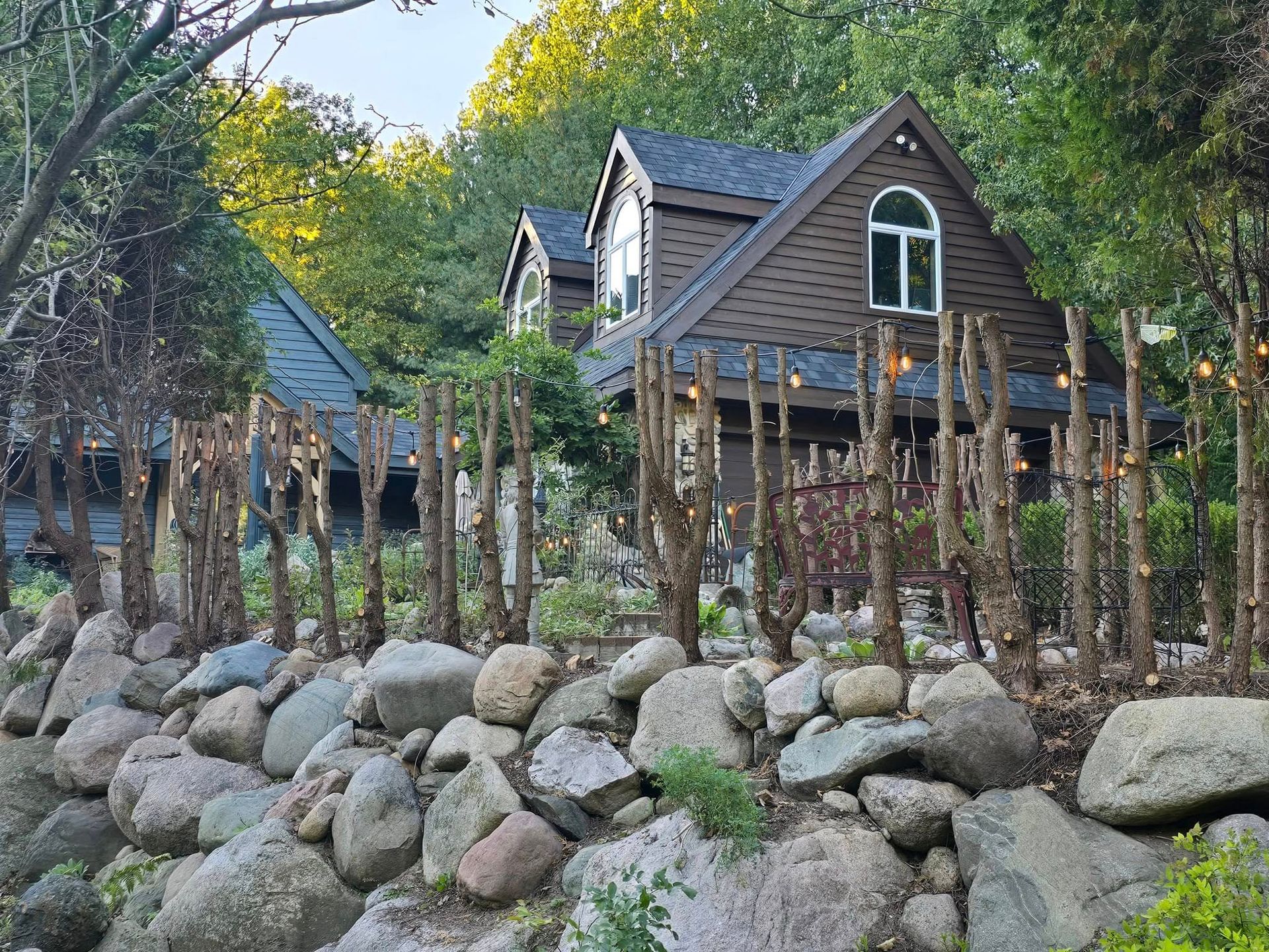 A house surrounded by trees and rocks with a stone wall in front of it.