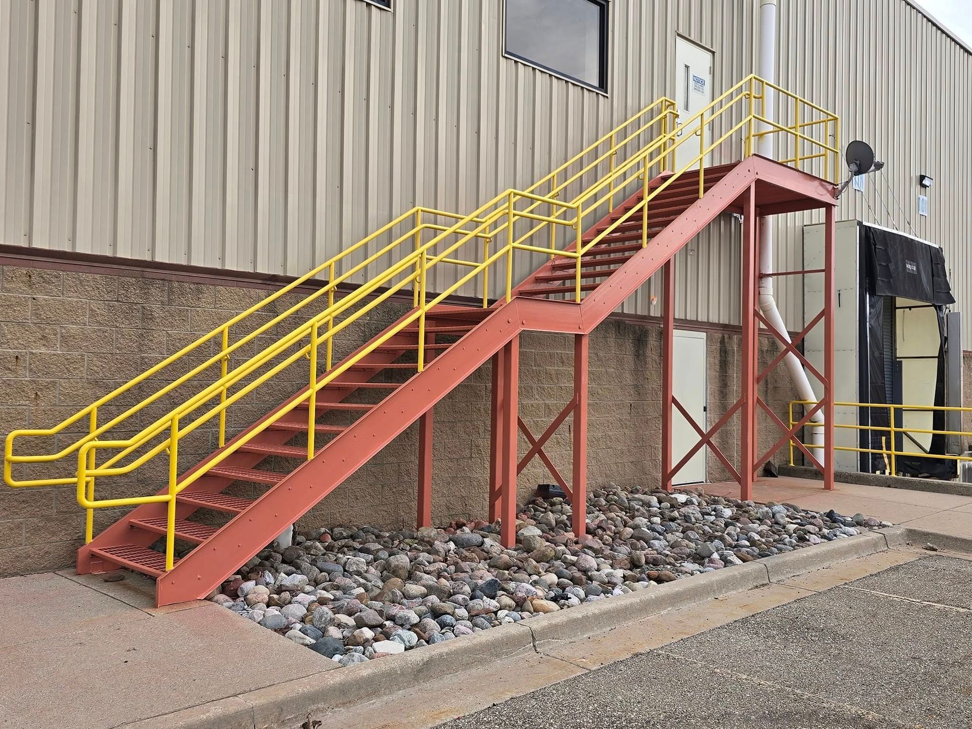 A red staircase with a yellow railing is outside of a building.