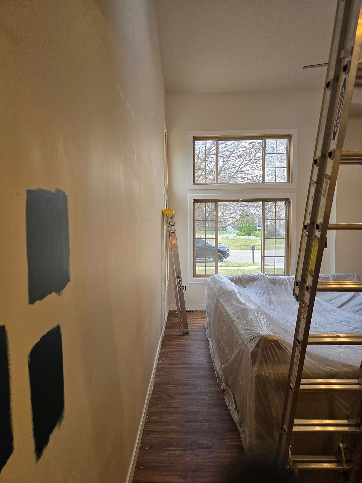 A living room with a ladder and a couch covered in plastic.