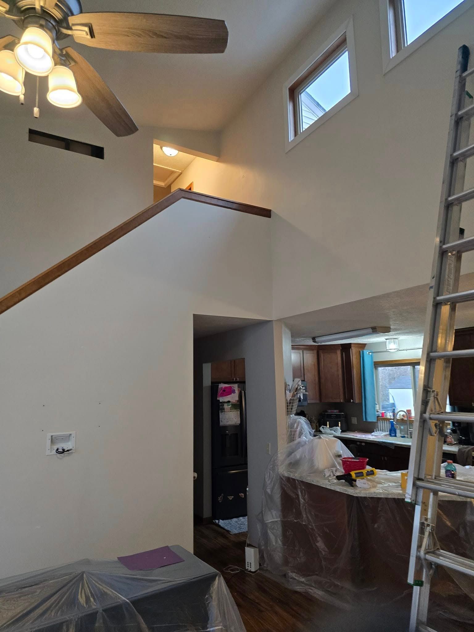A living room with a ceiling fan and a ladder.