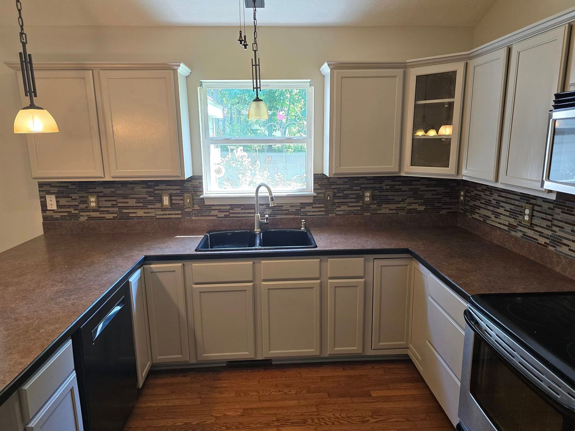 A kitchen with white cabinets , granite counter tops , black appliances and a window.
