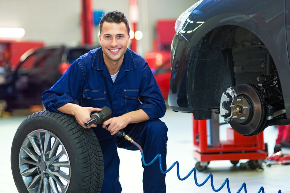 tire expert posing with a replacement tire in an auto repair shop