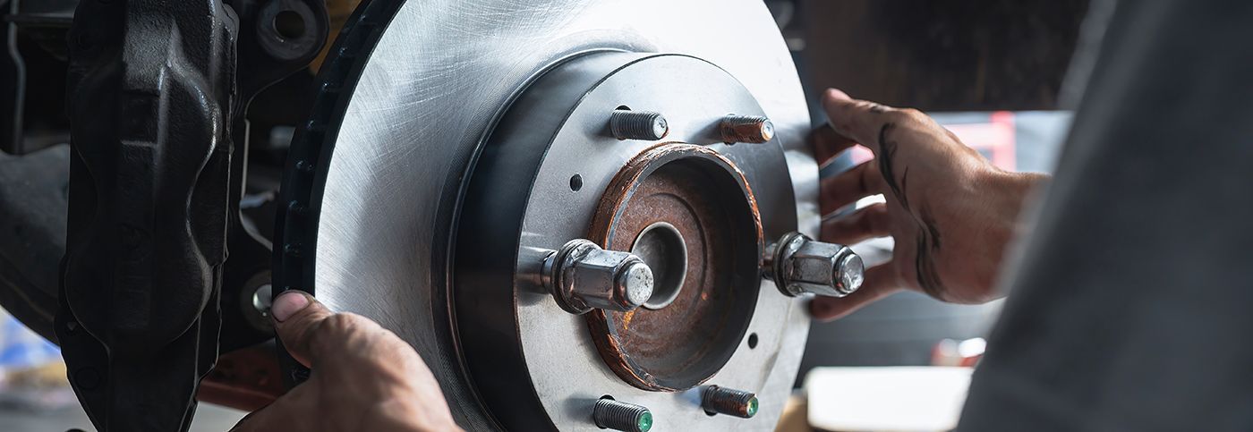 Hands installing a brake rotor on a car wheel assembly.