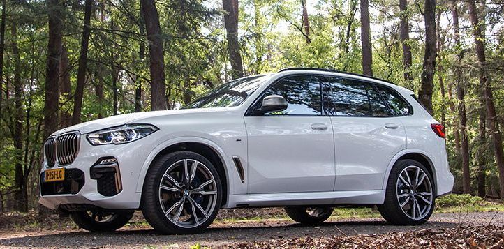 A white bmw x5 is parked in the middle of a forest.