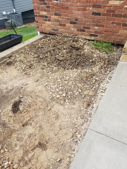 A pile of dirt is sitting on the sidewalk next to a brick wall.