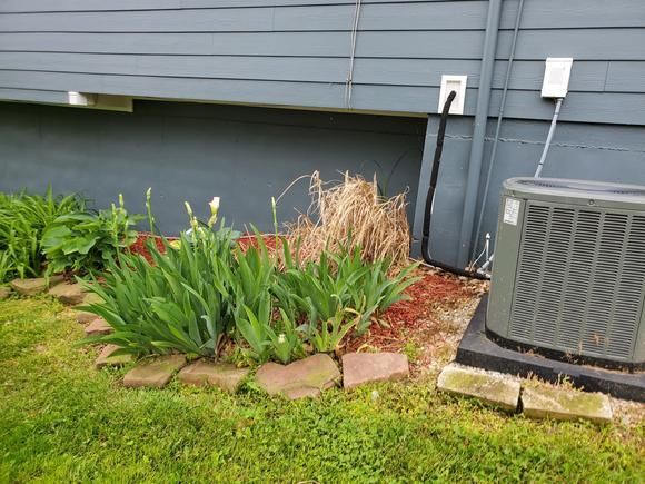 An air conditioner is sitting on the side of a house next to a garden.