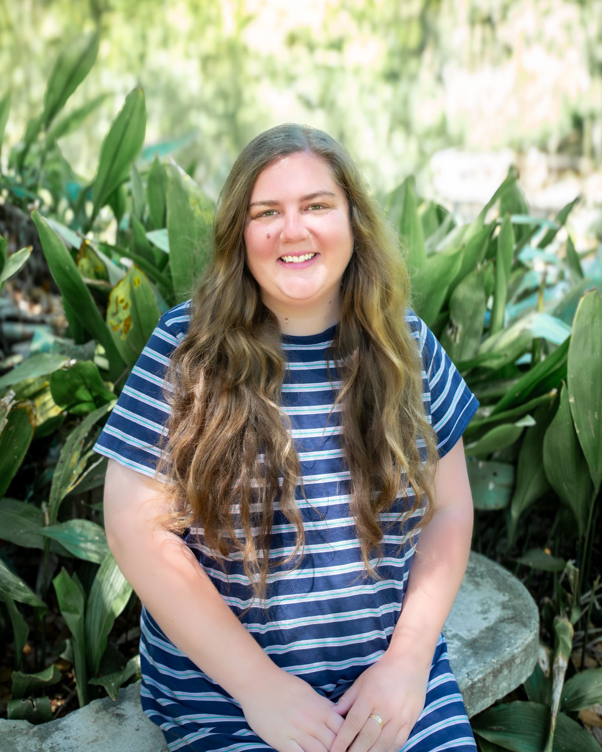 Smiling woman in a blue striped shirt standing among lush green plants outdoors