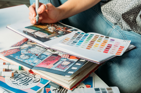 A picture of a person drawing in a art book on top of a white table.