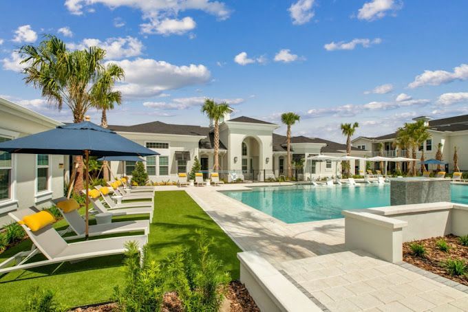 A large swimming pool surrounded by chairs and umbrellas in a residential area.