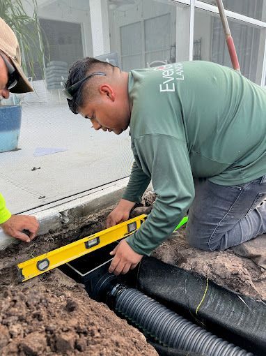 A man is kneeling down in the dirt with a yellow level.