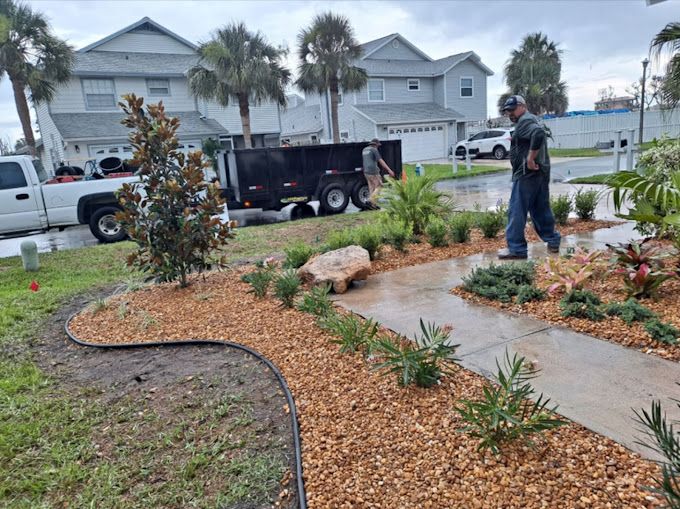 A man is standing on a sidewalk next to a lush green garden.