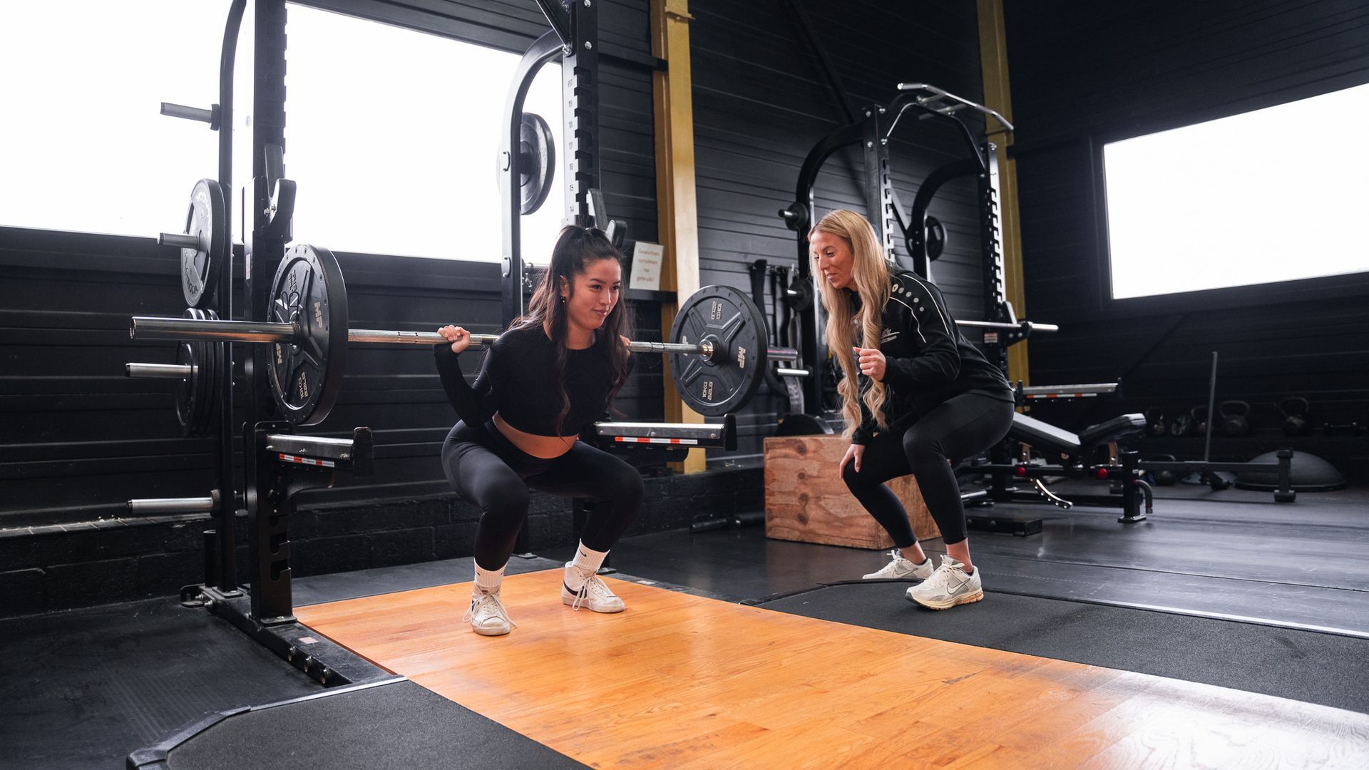 Twee vrouwen hurken met een halter in een sportschool.
