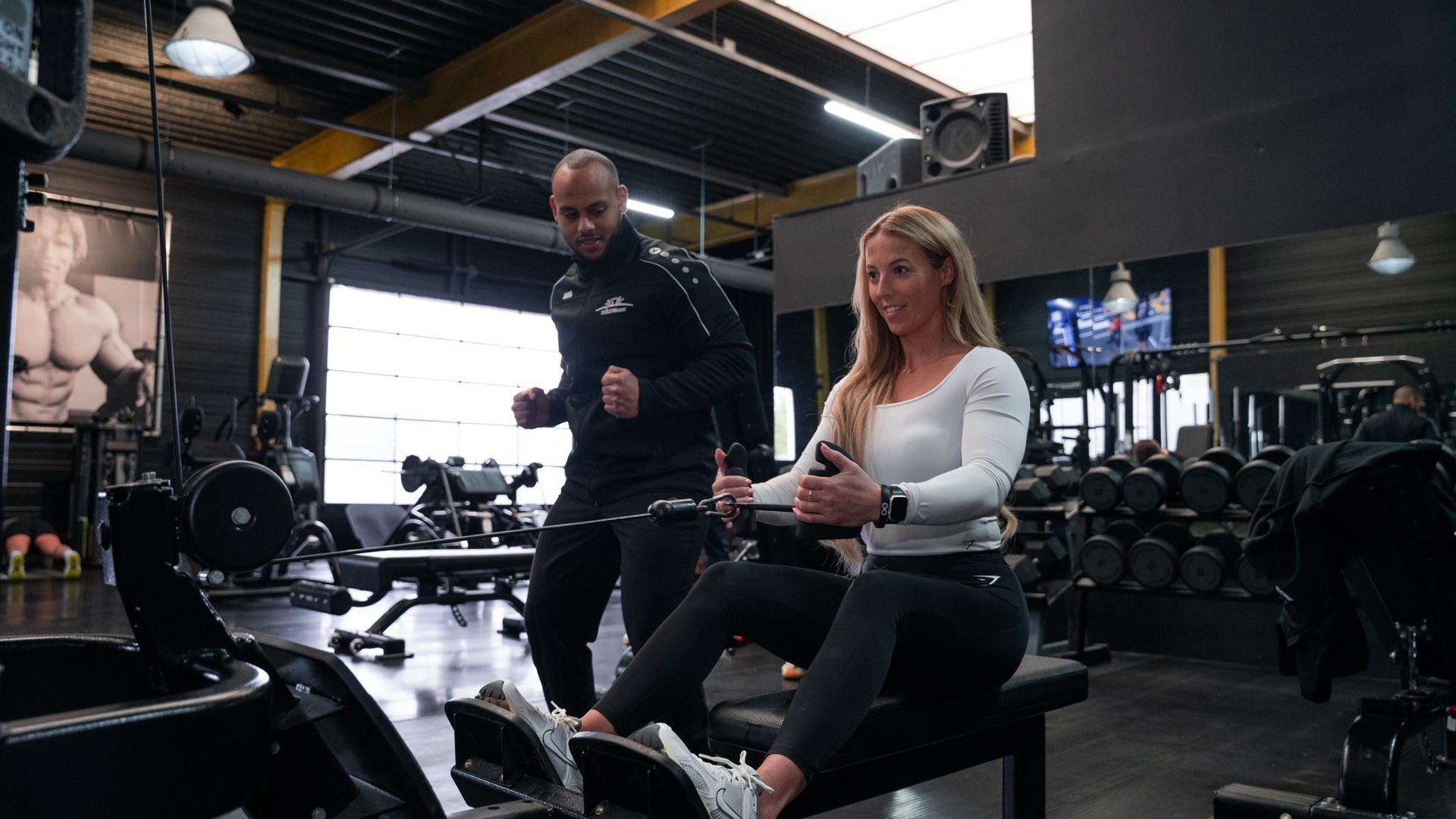 Een man leert een vrouw hoe ze een roeimachine moet gebruiken in een sportschool.
