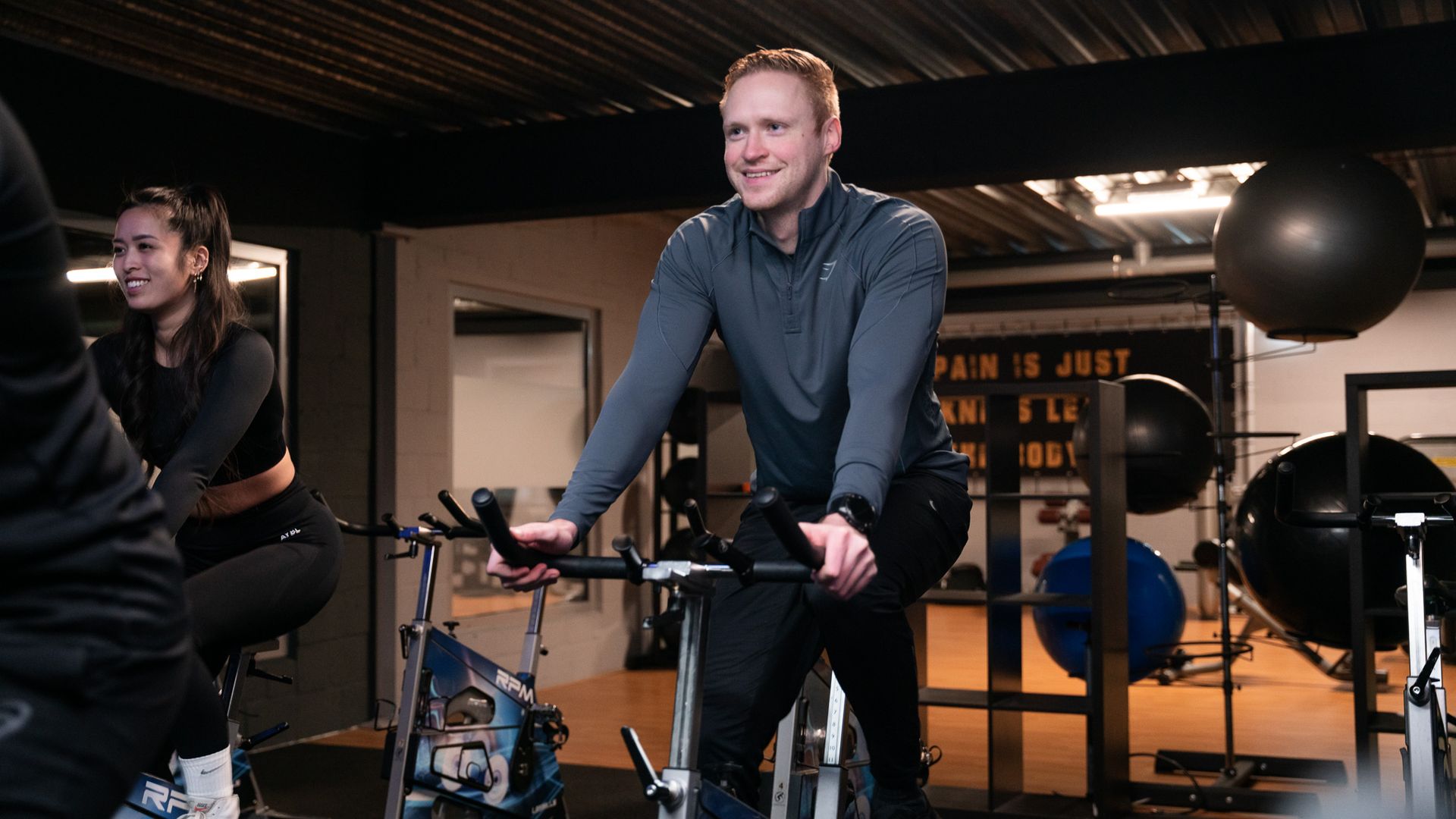 Een man en een vrouw fietsen op een hometrainer in een sportschool.