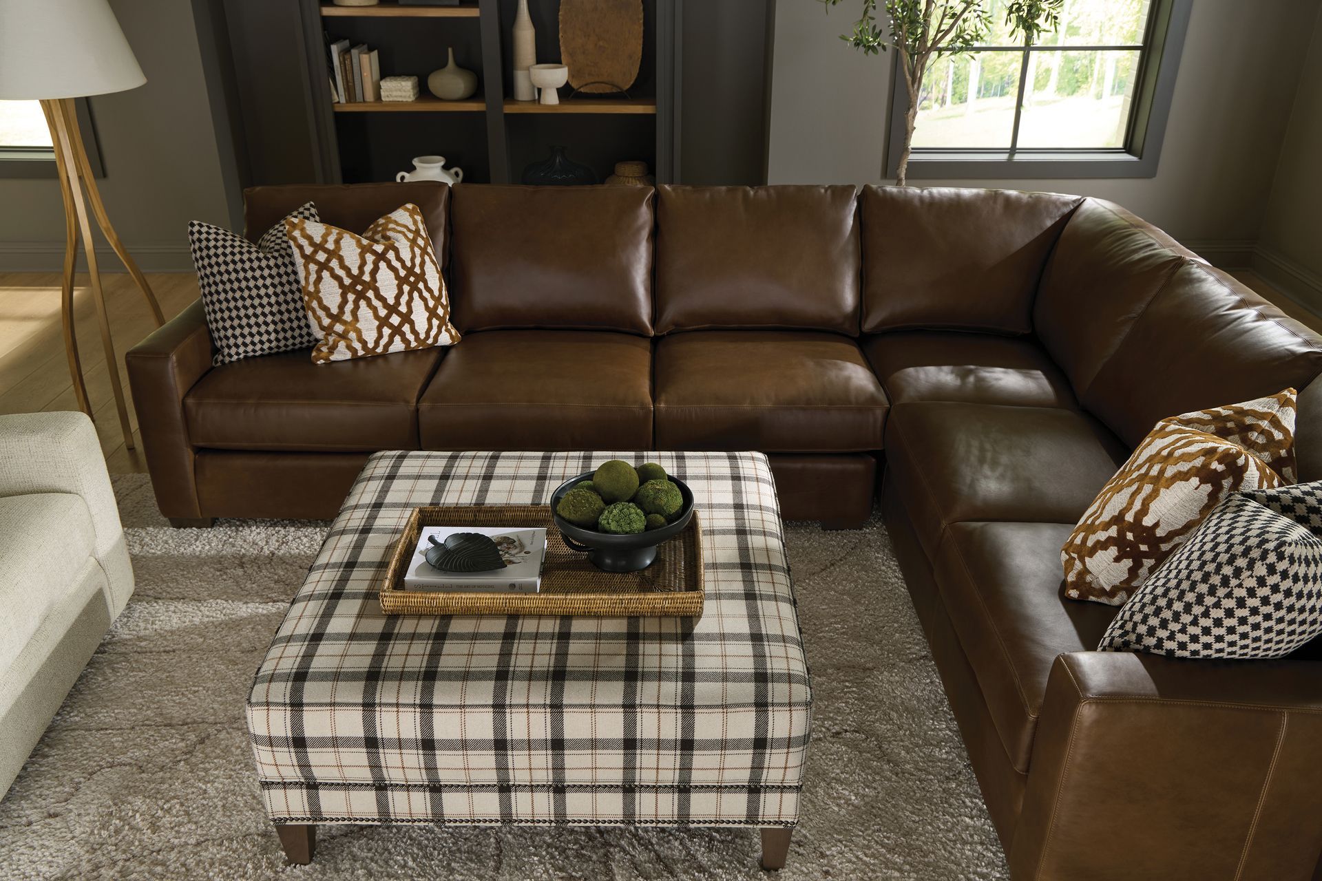 Brown leather sectional sofa with patterned pillows, plaid ottoman coffee table.