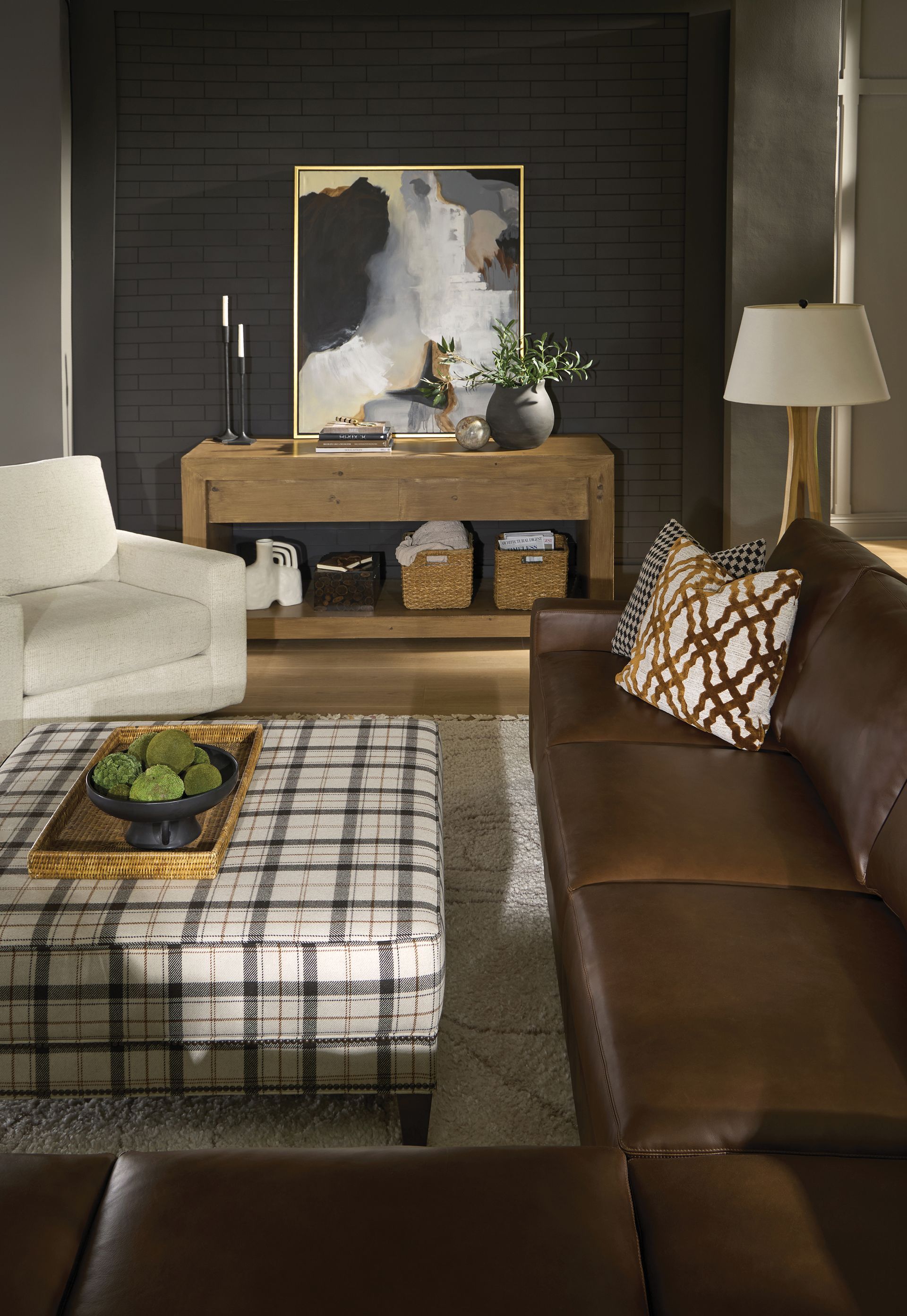 Living room with brown leather sofa, patterned ottoman, wooden console, and abstract art.