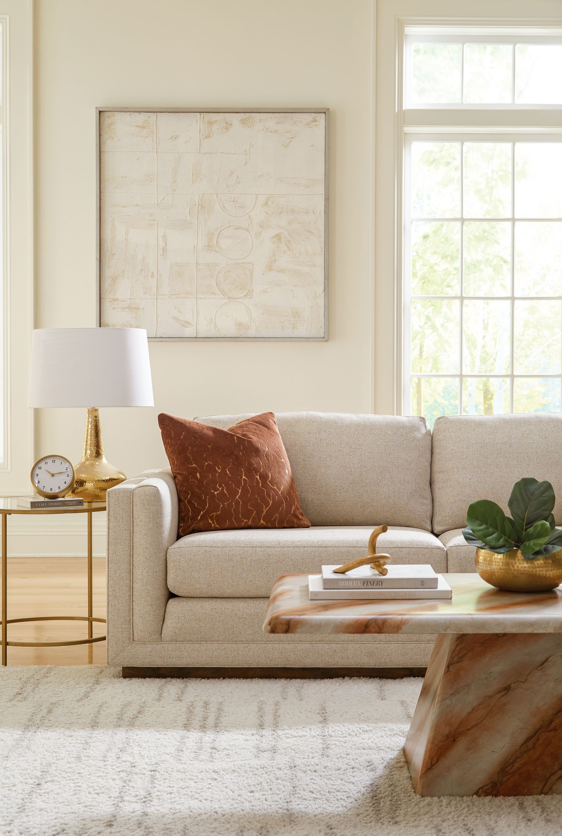 Living room with a cream-colored couch, art, and a coffee table. Sunlight streams in from a window.