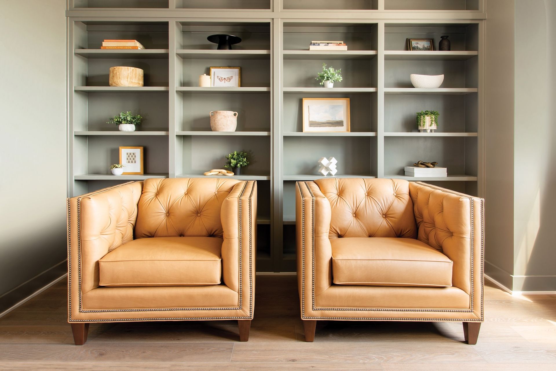 Two tan leather armchairs in front of a gray built-in bookshelf filled with decor.