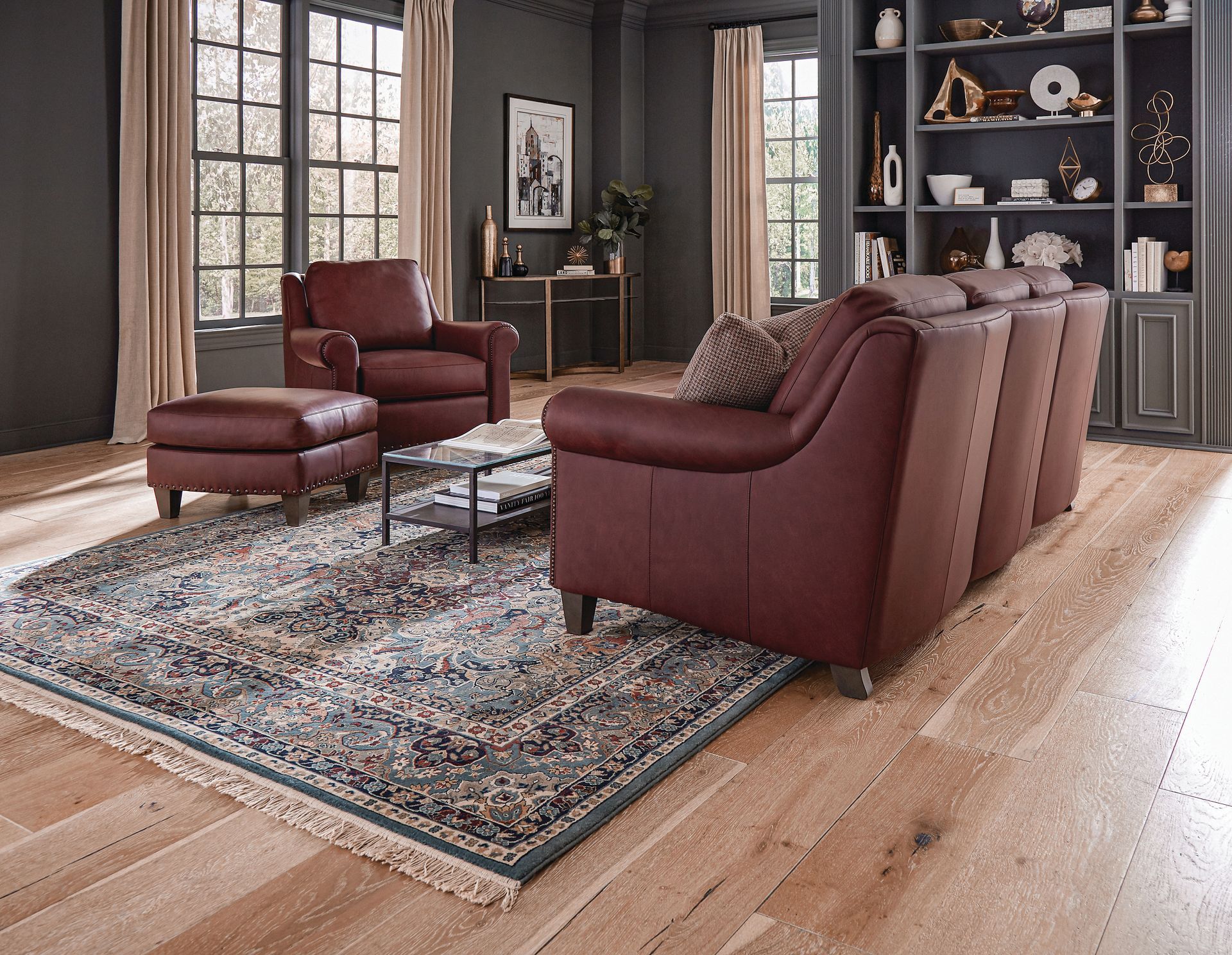 Living room with burgundy leather furniture, rug, hardwood floor, and built-in shelves.