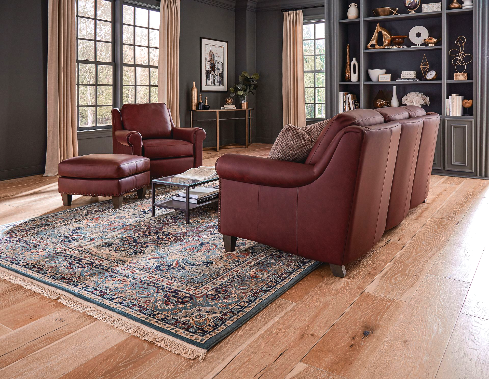 Living room with red leather sofa, armchair, and ottoman on a patterned rug, hardwood floors, and built-in shelves.