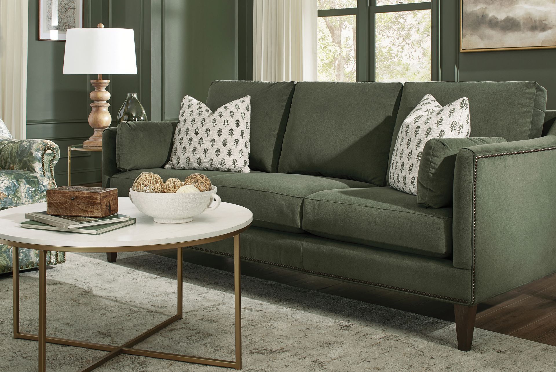 Green sofa with patterned pillows in a living room, next to a marble-topped coffee table.